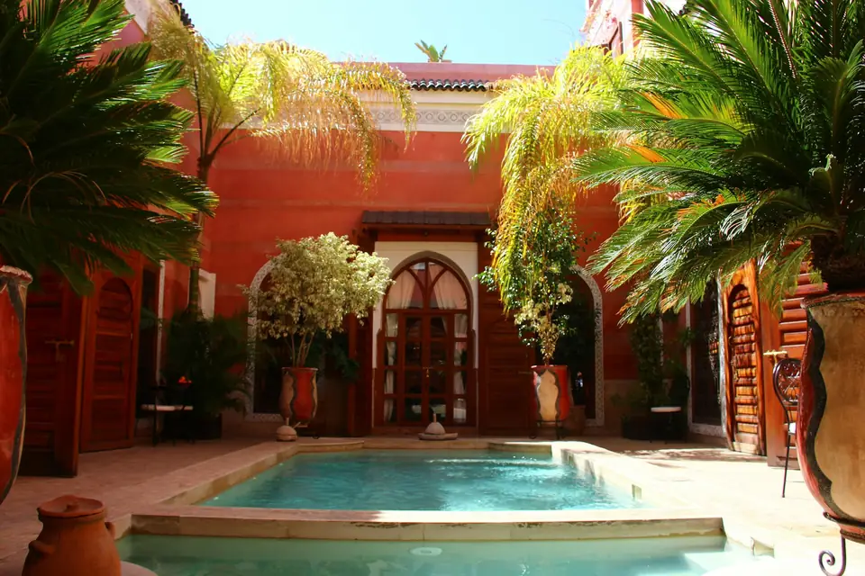 Patio de riad aux murs ocre rouge, avec bassin et palmiers